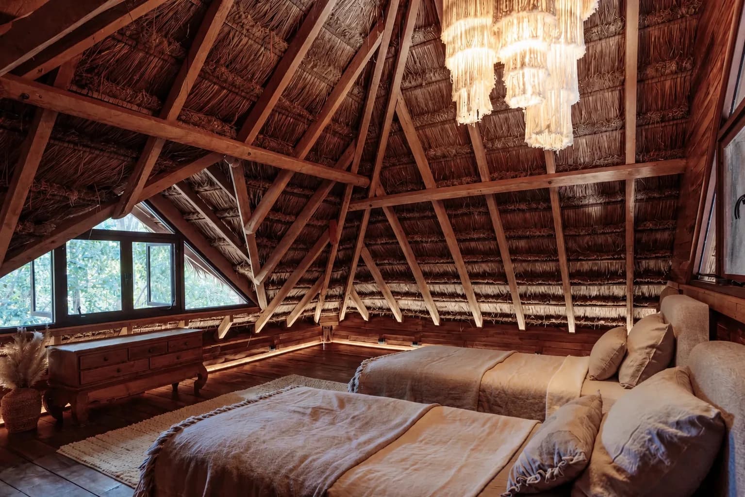 The Lodge upstairs sleeping loft with two beds under a thatched palapa roof and chandelier